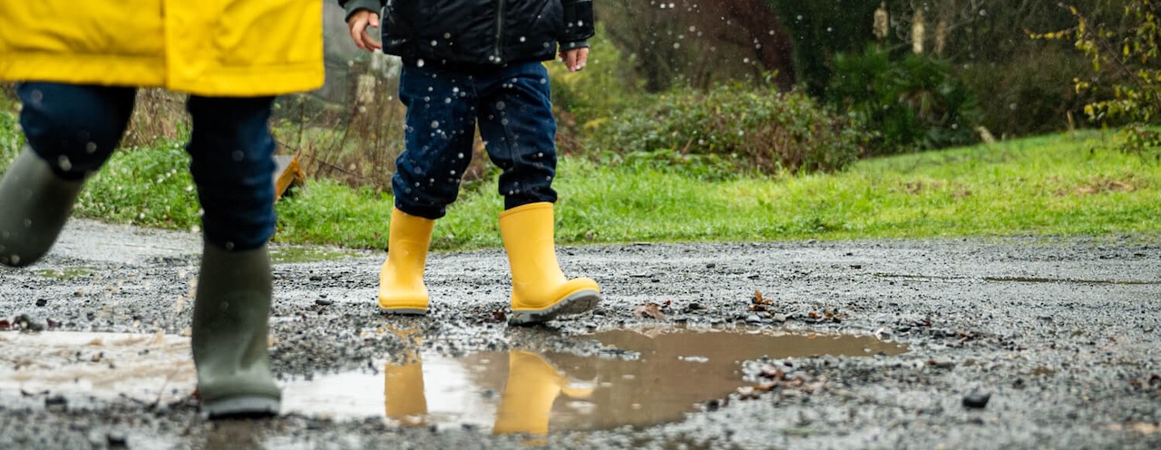 Kinder tapsen mit Gummistiefeln durch eine Regenpfütze